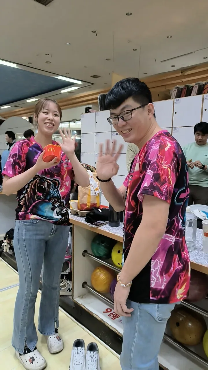 兩位球友穿著桃紅紫色地獄鎖鍊爆力熊保齡球衣，在球館裡揮手