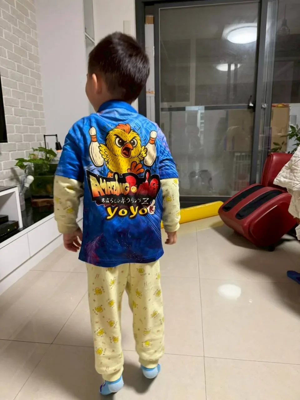 小朋友穿著藍色小雞圖案的兒童保齡球服，在家裡的背影
